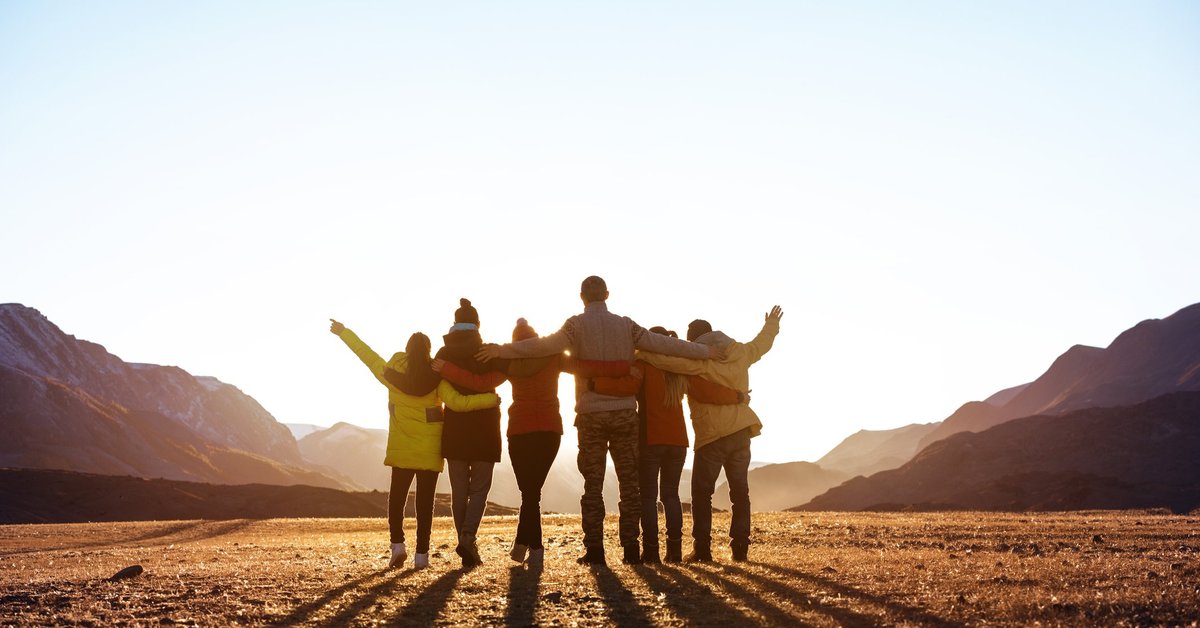 A group of friends looking at the sunset with their arms around each other.