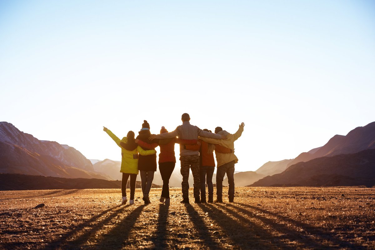 A group of friends looking at the sunset with their arms around each other.