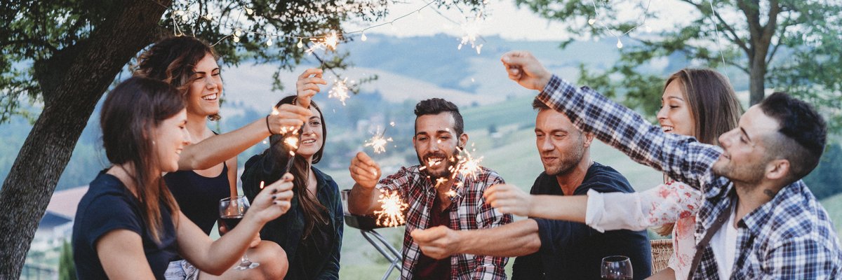 Group of young adults holding sparklers while having an outdoor picnic.