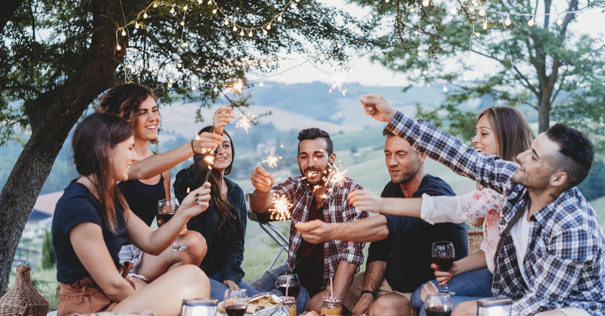 Group of young adults holding sparklers while having an outdoor picnic.