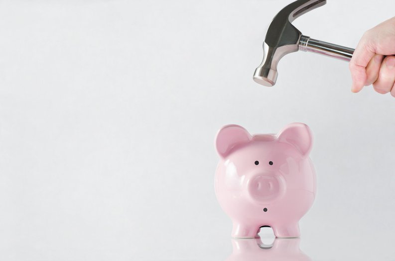 A hand holding a hammer over a worried-looking piggy bank.