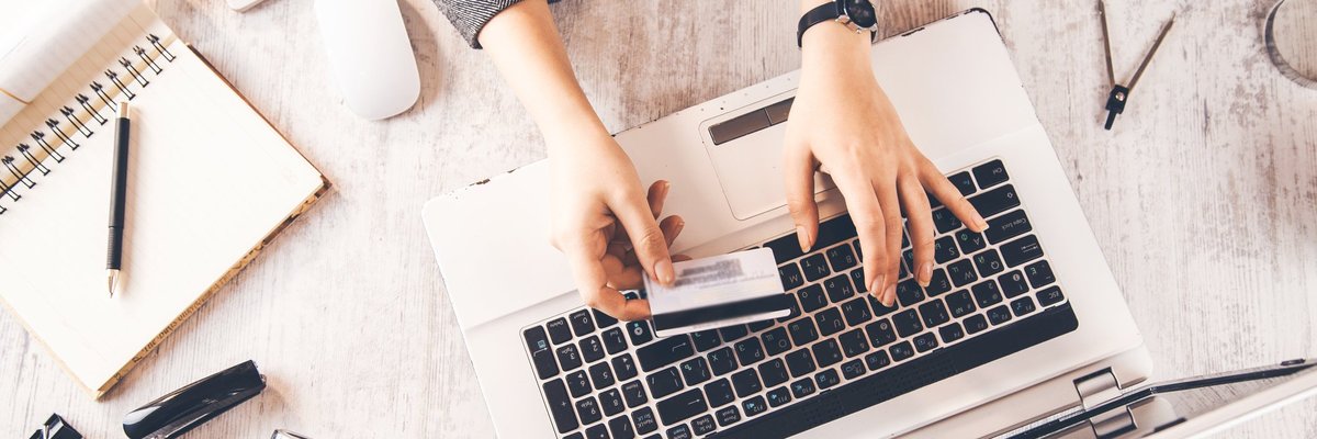 A pair of hands holding a credit card and typing on a laptop.