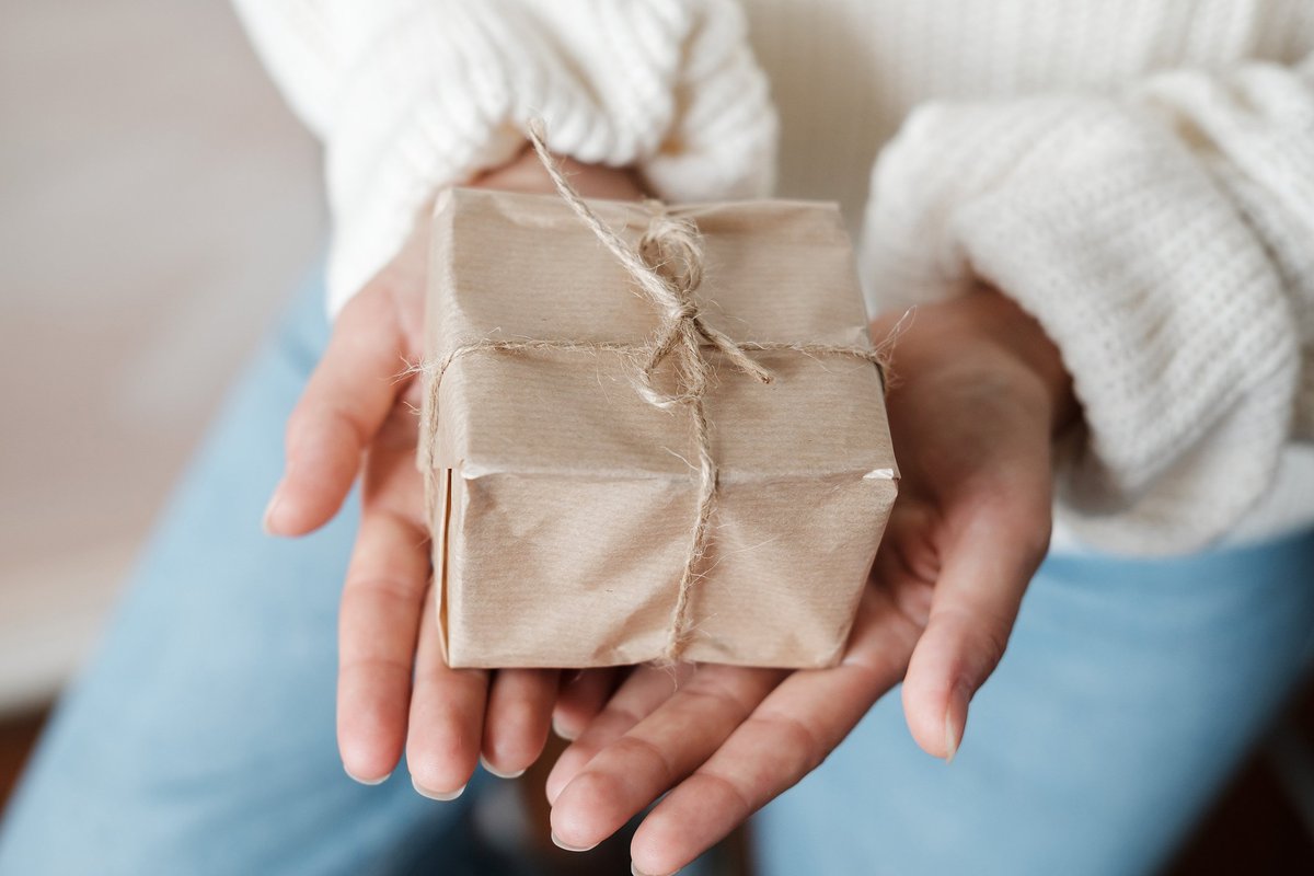 Hands offering out a gift wrapped in brown paper and twine.