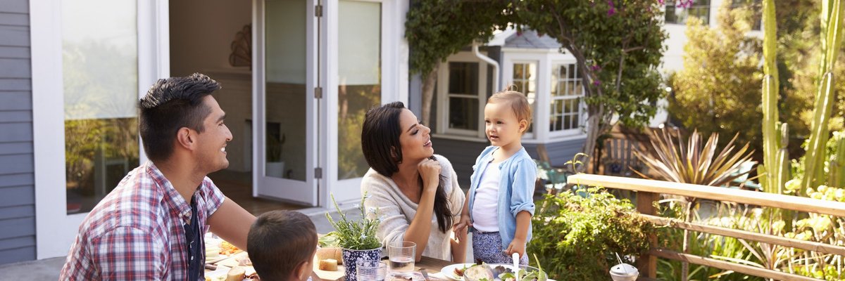 Two parents with their young children having lunch at a picnic table on their back deck.