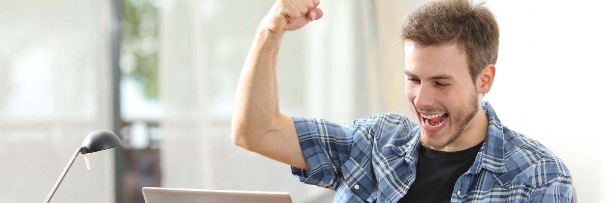Happy man looking at laptop with fist raised in the air.