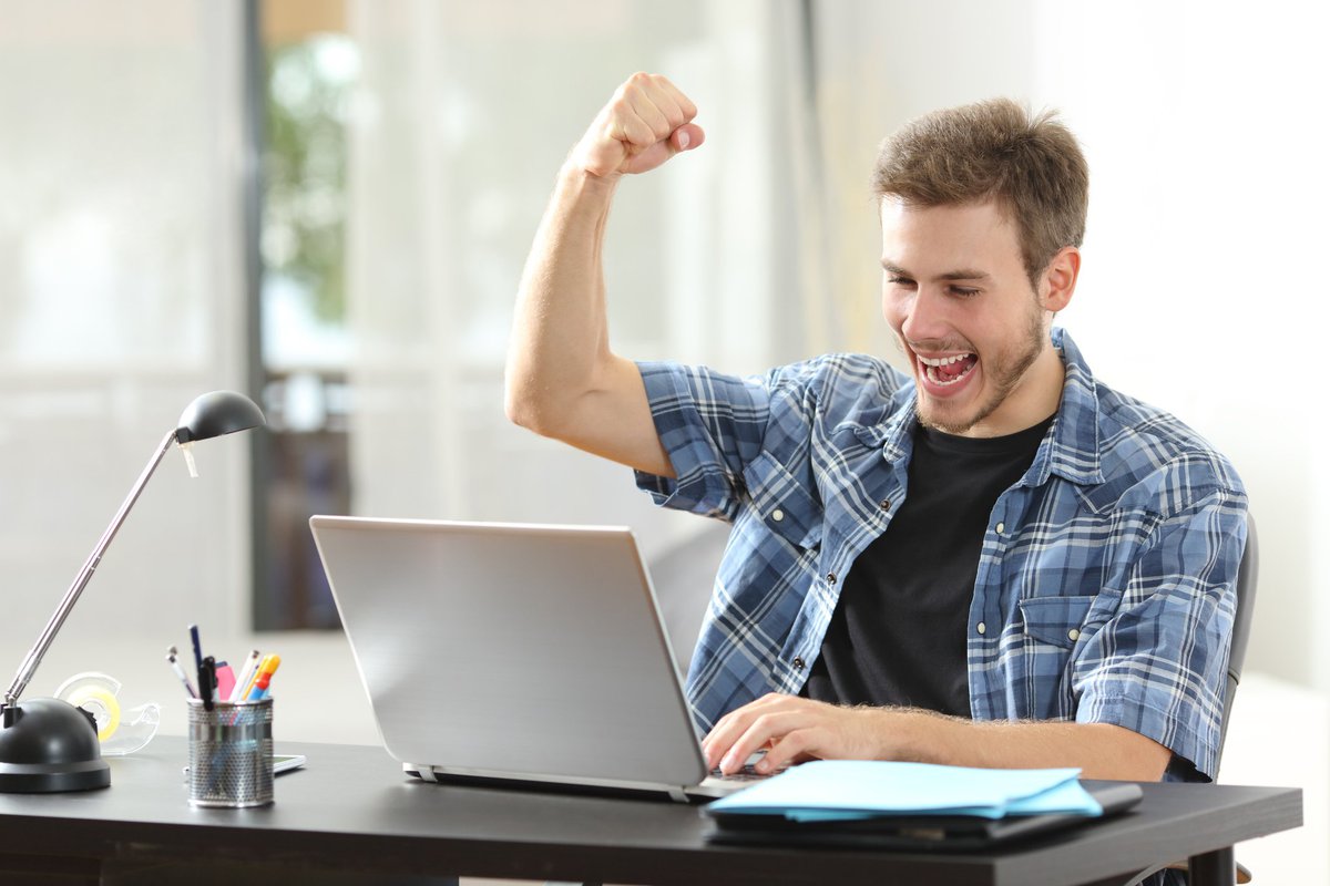 Man looking at laptop screen and raising his fist in celebration.
