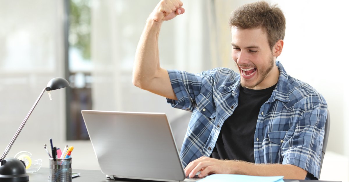 Happy man looking at laptop with fist raised in the air.