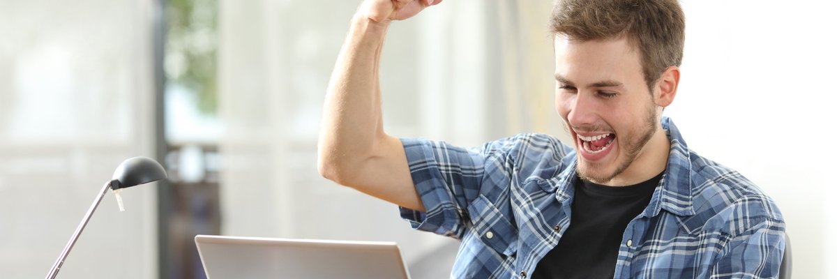 Happy man looking at laptop with fist raised in the air.