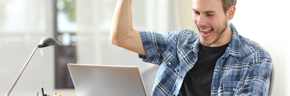 Happy man at laptop raises his fist in the air.