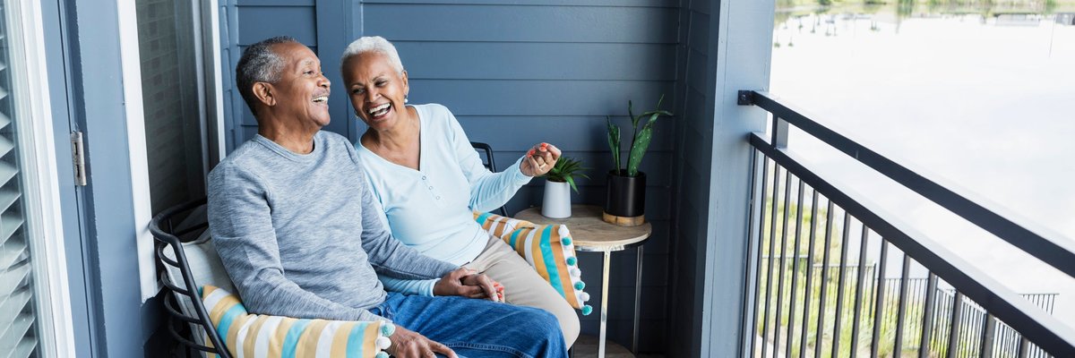 Happy mature couple sitting on balcony overlooking a pond.