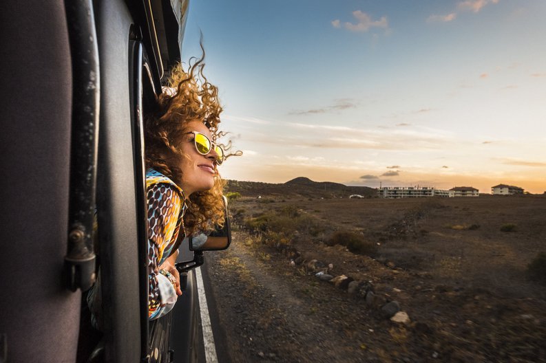 A young woman smiling with her head out leaning out of a train window at dusk.