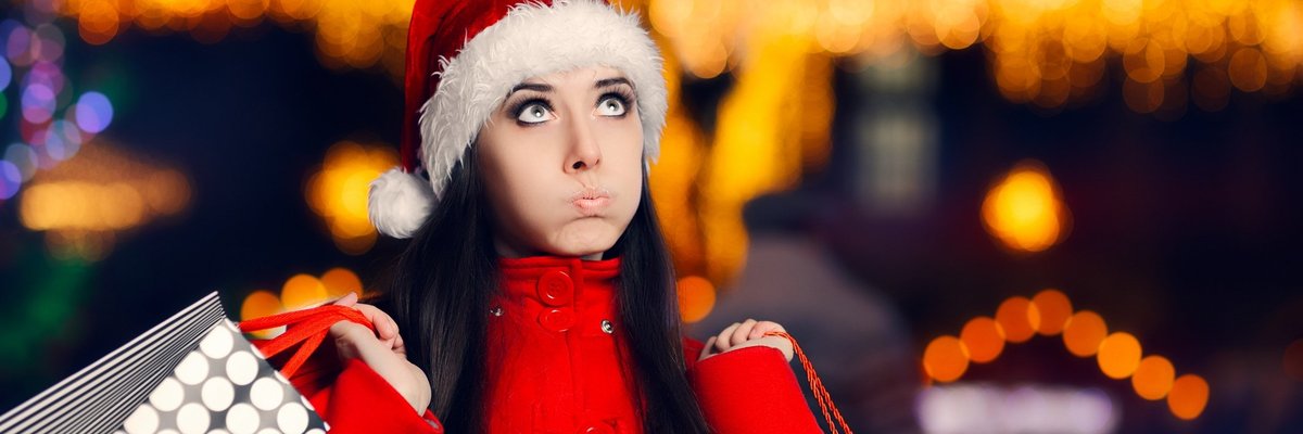 Woman in santa hat pursing her lips as she carries shopping bags.