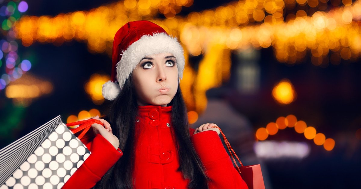 Woman in santa hat pursing her lips as she carries shopping bags.