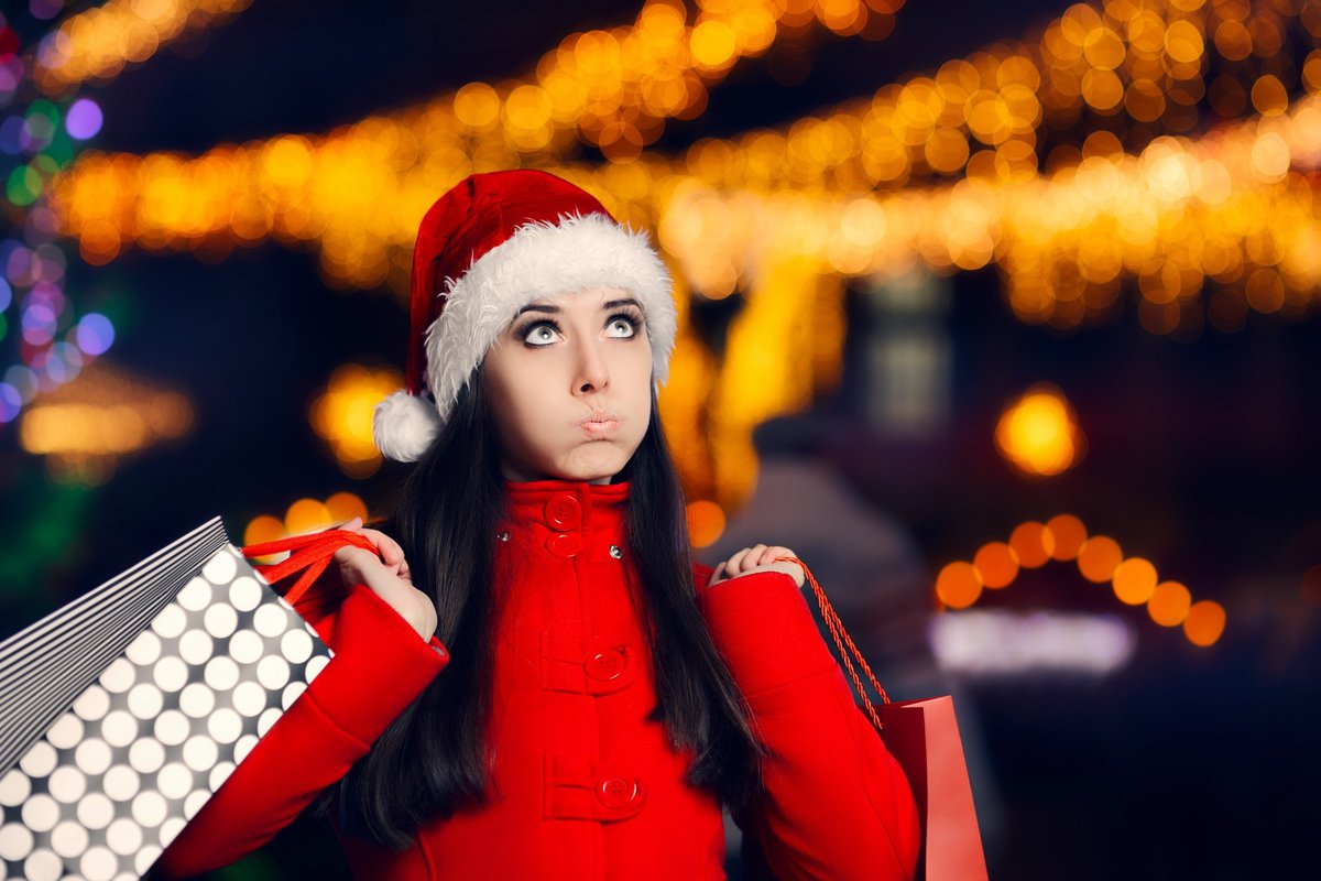 Woman in santa hat pursing her lips as she carries shopping bags.