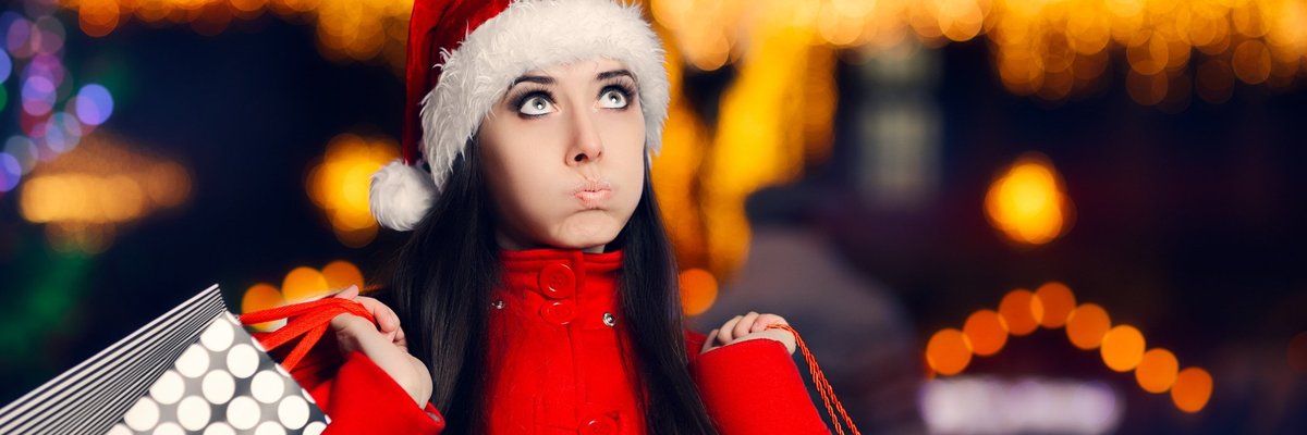 Woman in santa hat pursing her lips as she carries shopping bags.