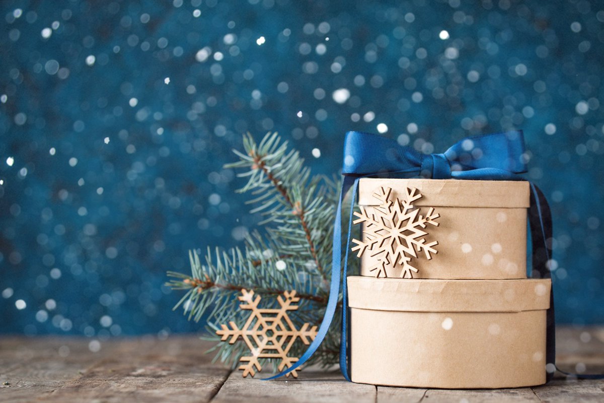 Wrapped gift boxes decorated with a blue bow, wooden snowflakes, and a pine branch.