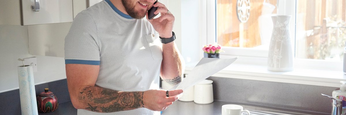 A homeowner stands in his kitchen and is on the phone with his loan servicer.