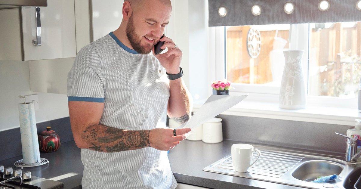 A homeowner stands in his kitchen and is on the phone with his loan servicer.
