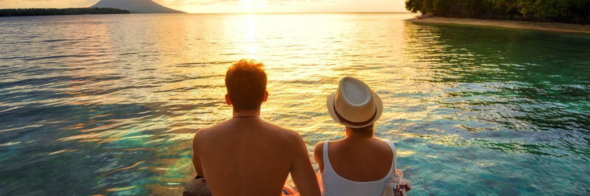 Couple sitting over the water watching a tropical sunset
