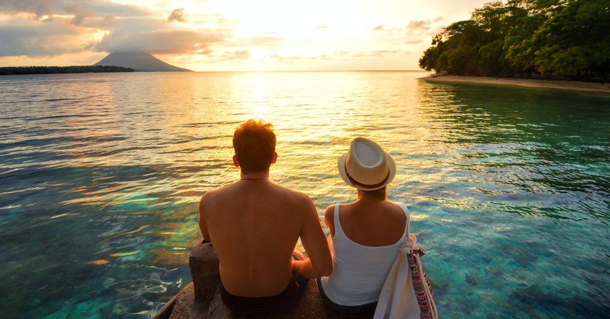 Couple sitting over the water watching a tropical sunset