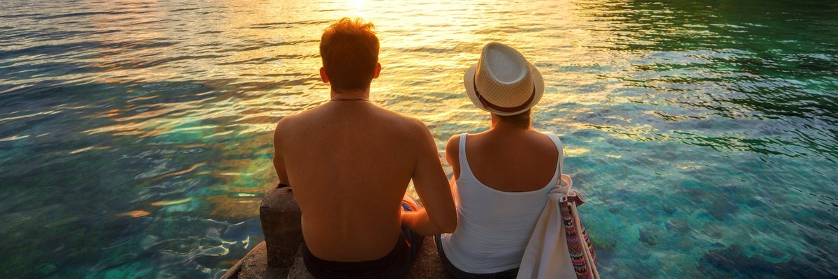 Couple sitting over the water watching a tropical sunset