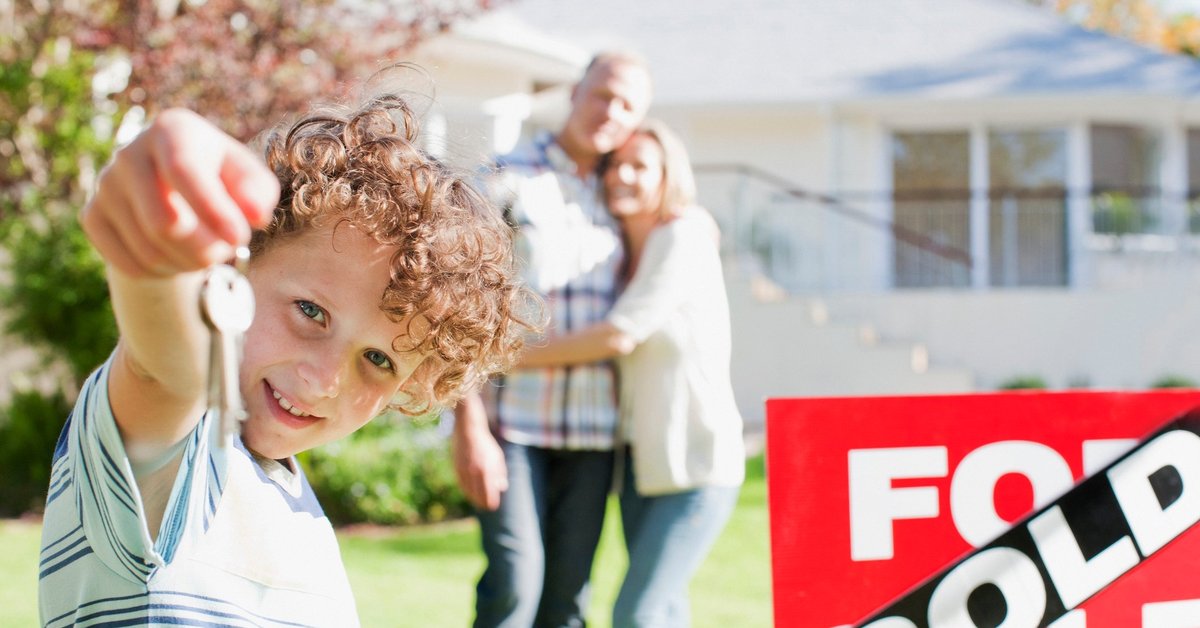 Family standing in front of sold house holding a key.