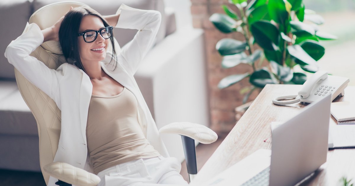 Content woman in glasses laying back in office chair with hands behind her head.