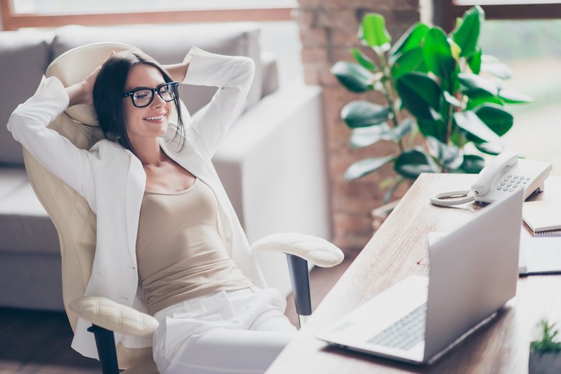 Content woman in glasses laying back in office chair with hands behind her head.