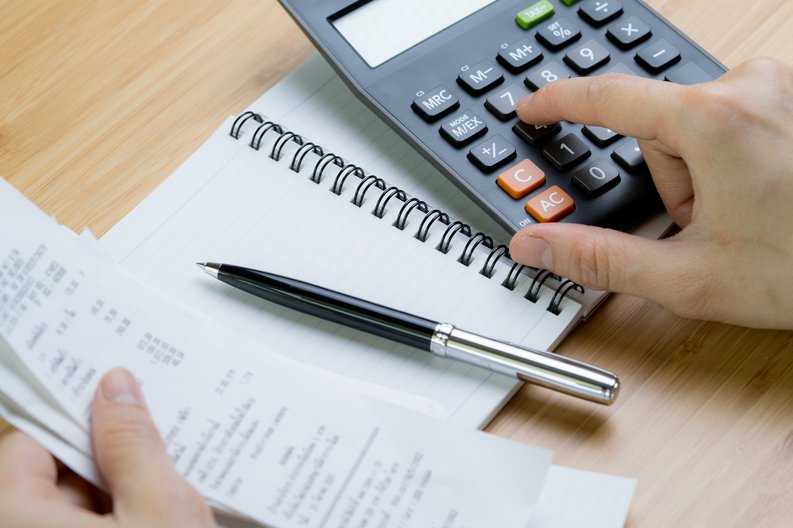 one hand types on a calculator while the other holds some receipts