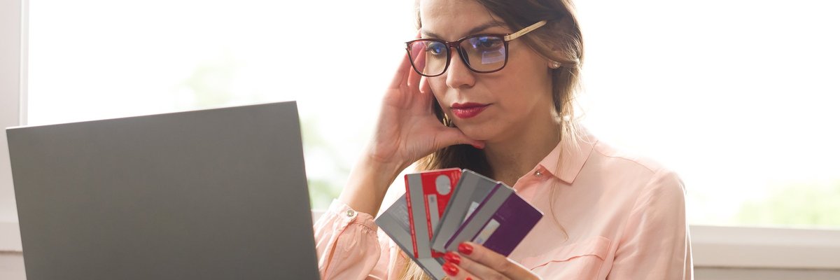 Stressed woman with handful of credit cards looking at laptop.