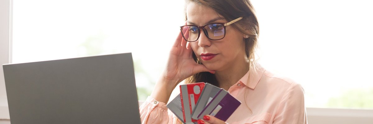 Stressed woman with handful of credit cards looking at laptop.