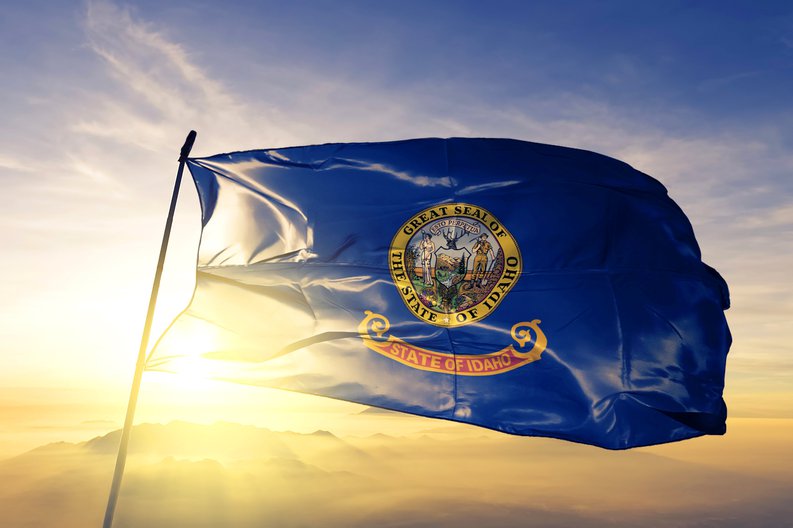 The Idaho state flag flying in front of a sunny sky.