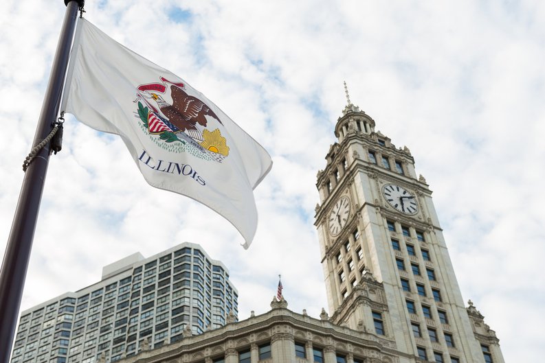 The Illinois state flag flying in front of buildings in Chicago.