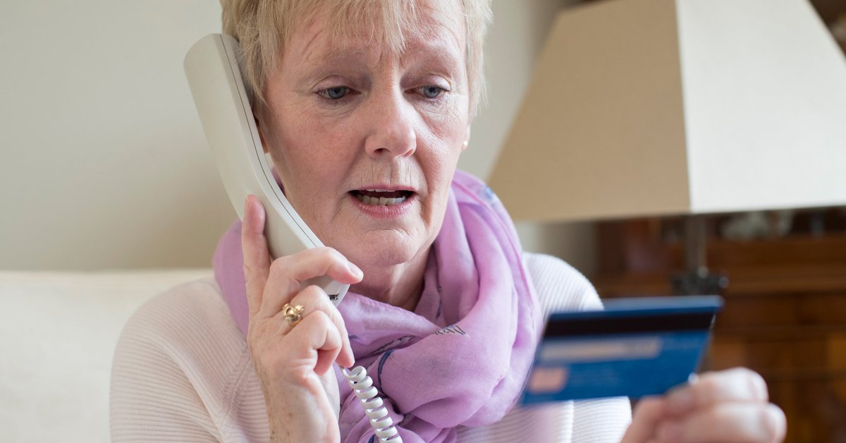 Concerned older woman looking at a credit card while on the phone.