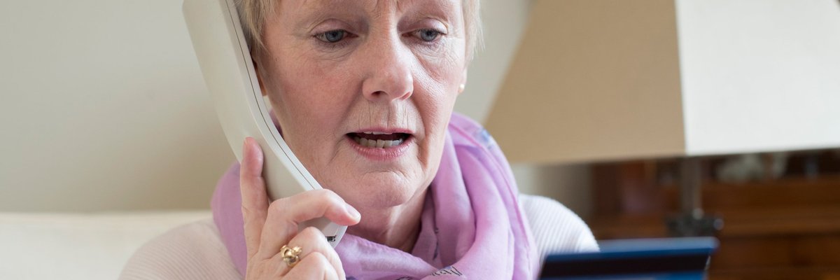 Concerned older woman looking at a credit card while on the phone.