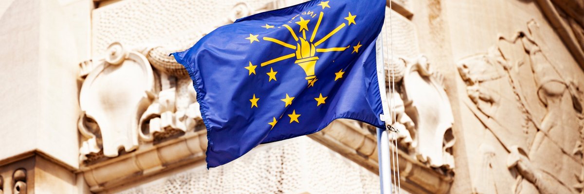 The Indiana state flag flying in front of a decorative building facade.