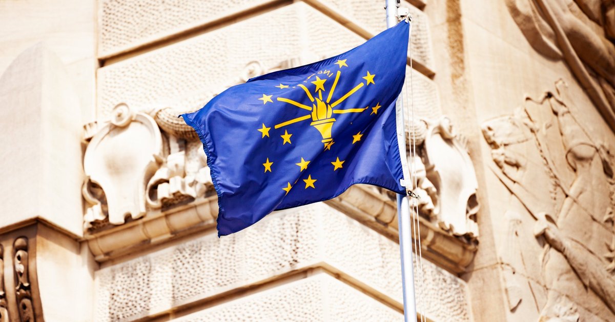 The Indiana state flag flying in front of a decorative building facade.