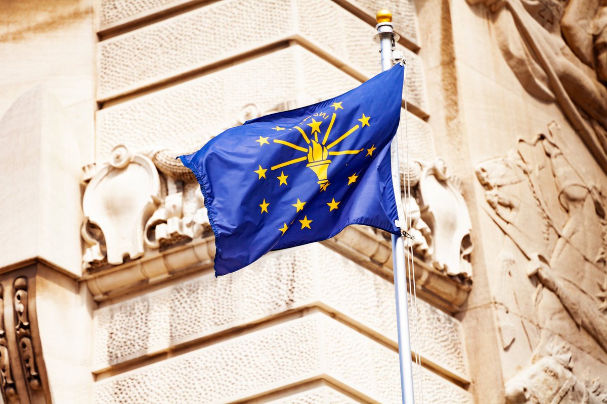 The Indiana state flag flying in front of a decorative building facade.