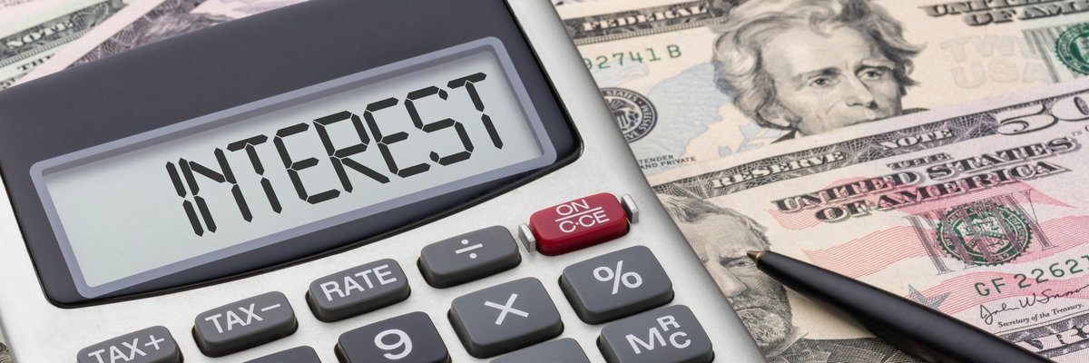 A calculator that says interest sitting on top of U.S. currency.