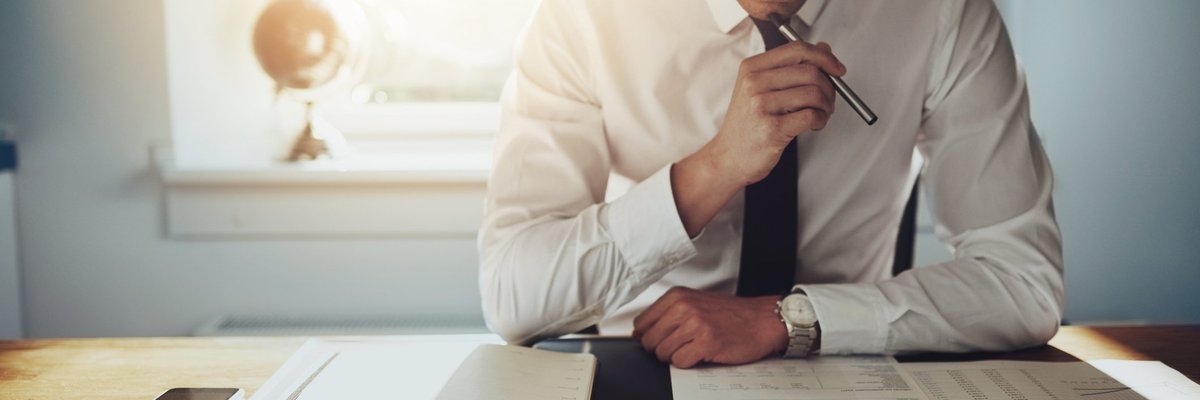 Man reading papers at a desk in a sunny office.