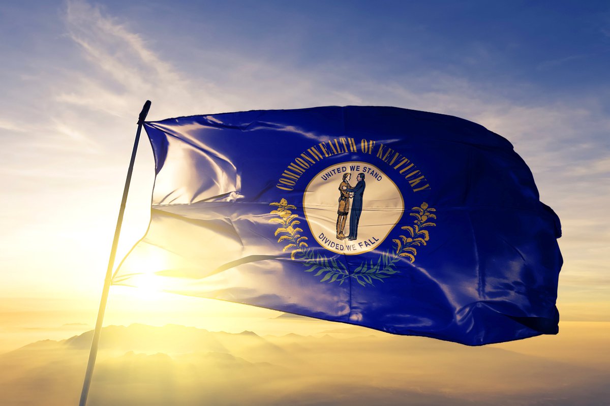 The Kentucky state flag flying in front of a sunny sky.