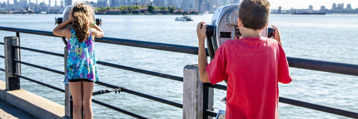 Kids looking at Manhattan Island through paying binoculars from the Liberty State Park in Jersey city during summer day.