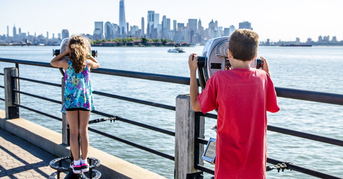 Kids looking at Manhattan Island through paying binoculars from the Liberty State Park in Jersey city during summer day.