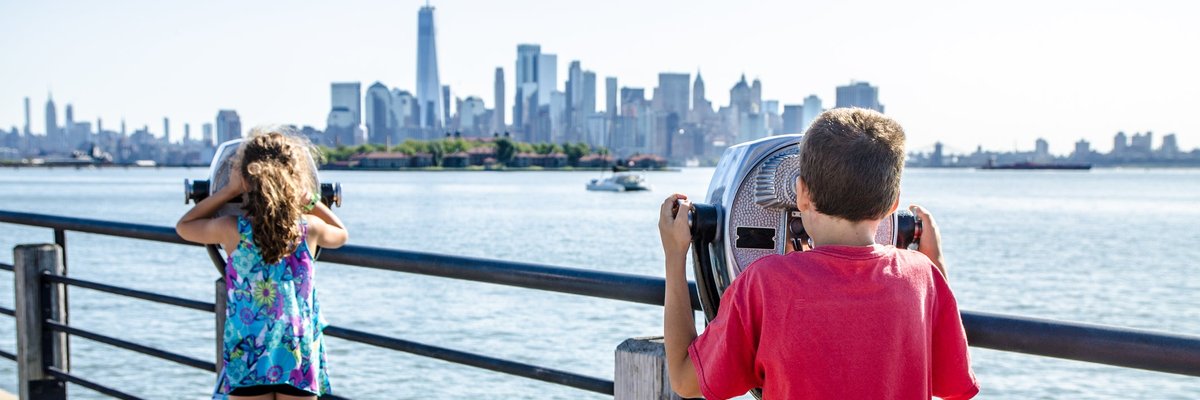 Kids looking at Manhattan Island through paying binoculars from the Liberty State Park in Jersey city during summer day.