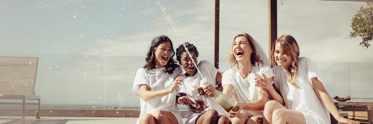 Four women popping bottle of champagne.