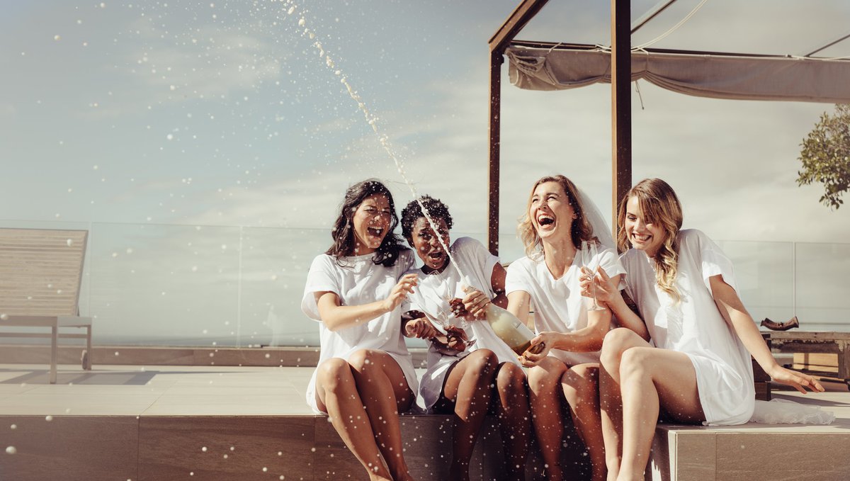 Four women popping bottle of champagne.