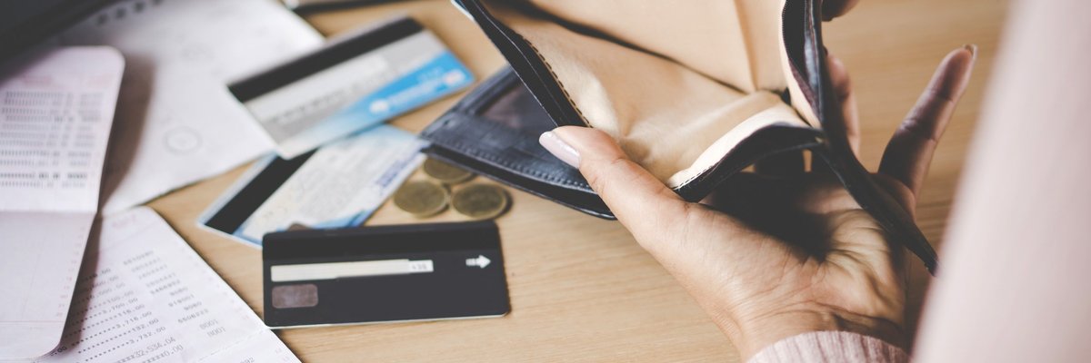 Woman looking at her empty wallet and a table with credit cards, coins, a calculator, and paperwork strewn about.