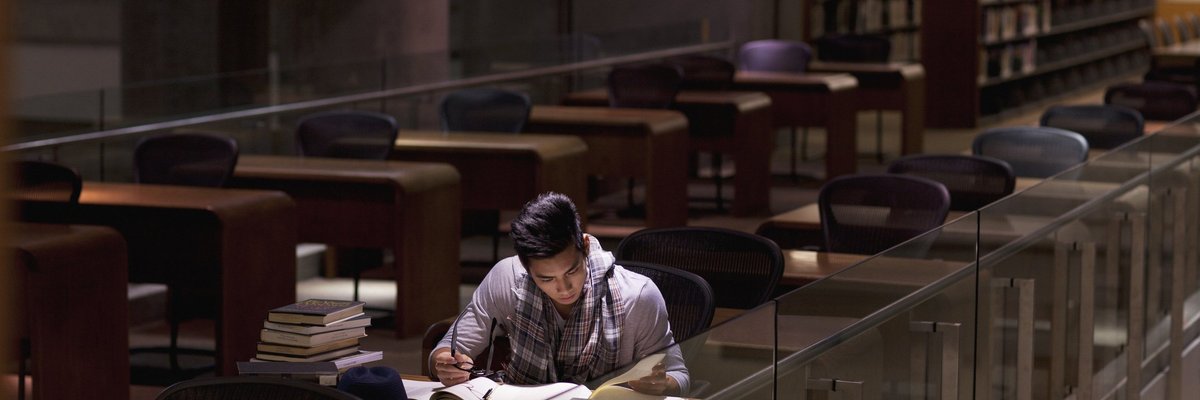 A male college student studying alone in a library.