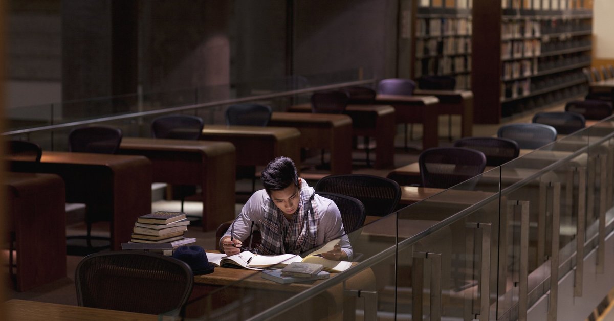 A male college student studying alone in a library.
