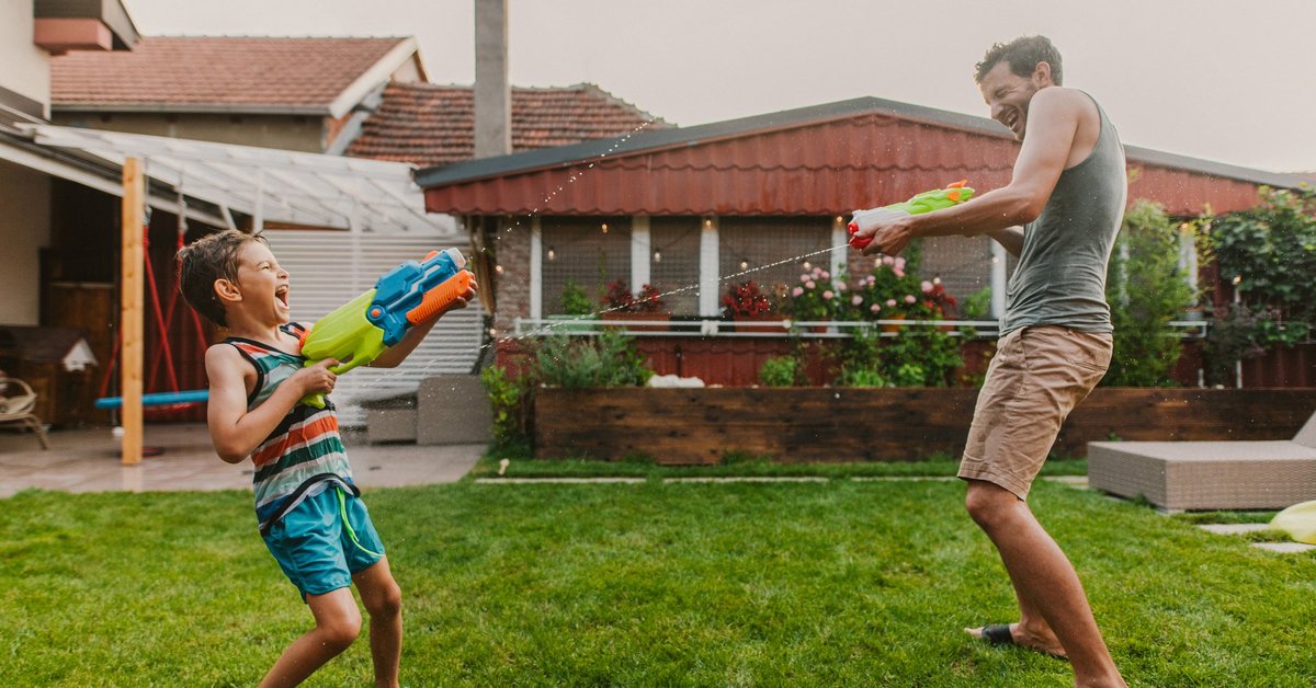 Man and child play with squirt guns in home's yard.